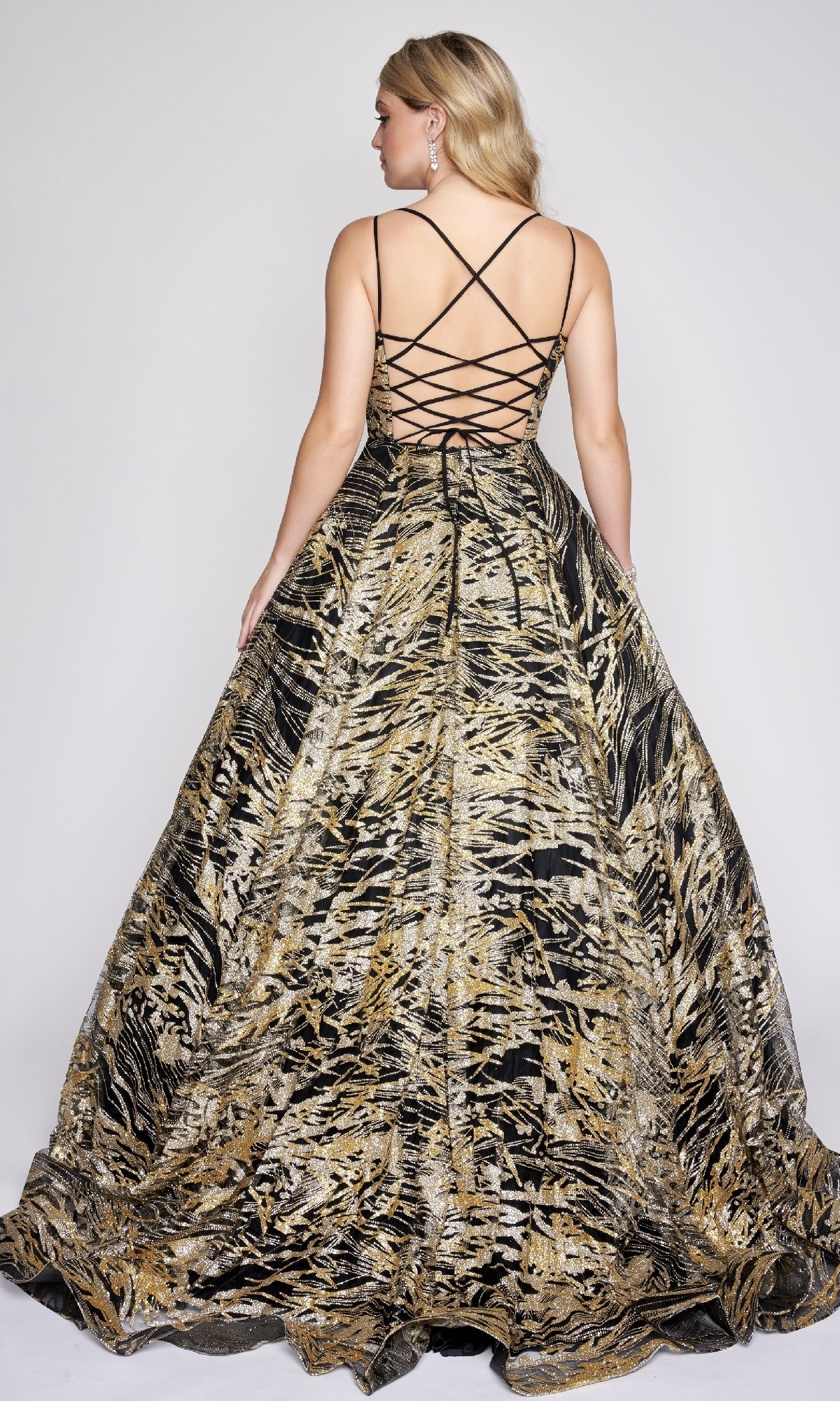 Woman wearing the Nina Canacci 8209 Print Prom Ball Gown in gold and black with a crisscross lace-up back, standing and facing away from the camera.